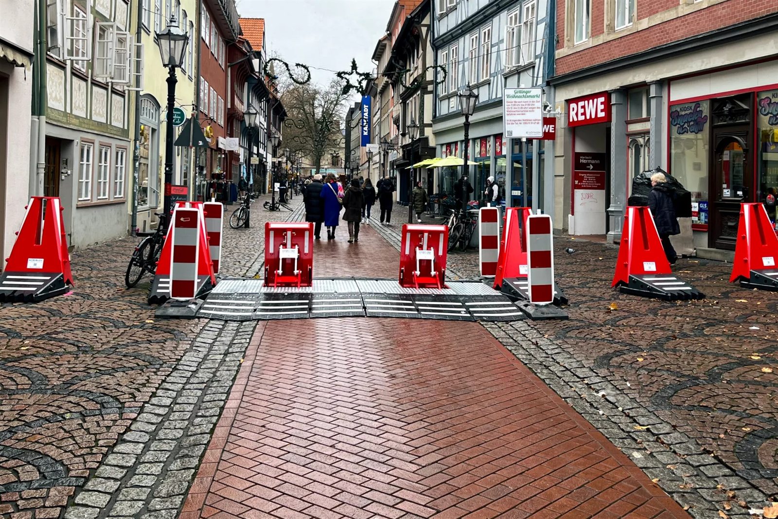 Durchlasssperre aus mobilen Fahrzeugsperren in einer Altstadtgasse mit Weihnachtsmarkt, dahinter Fußgänger
